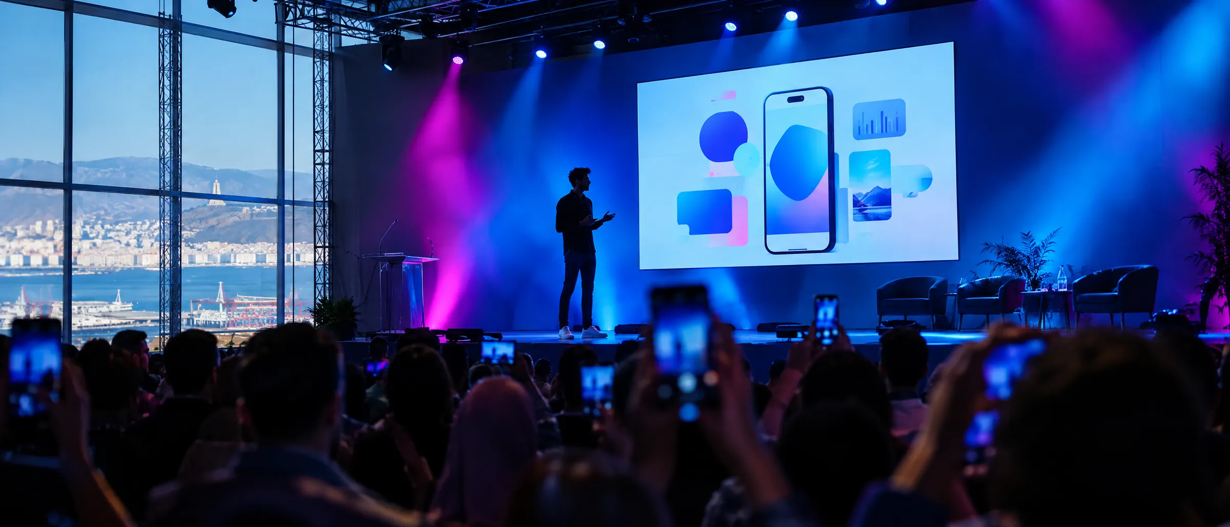 A startup pitch on a lit stage, audience filming with phones